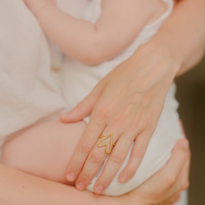 Close-up of a person holding a baby with a Aurore Havenne gold heart-shaped ring on one finger.