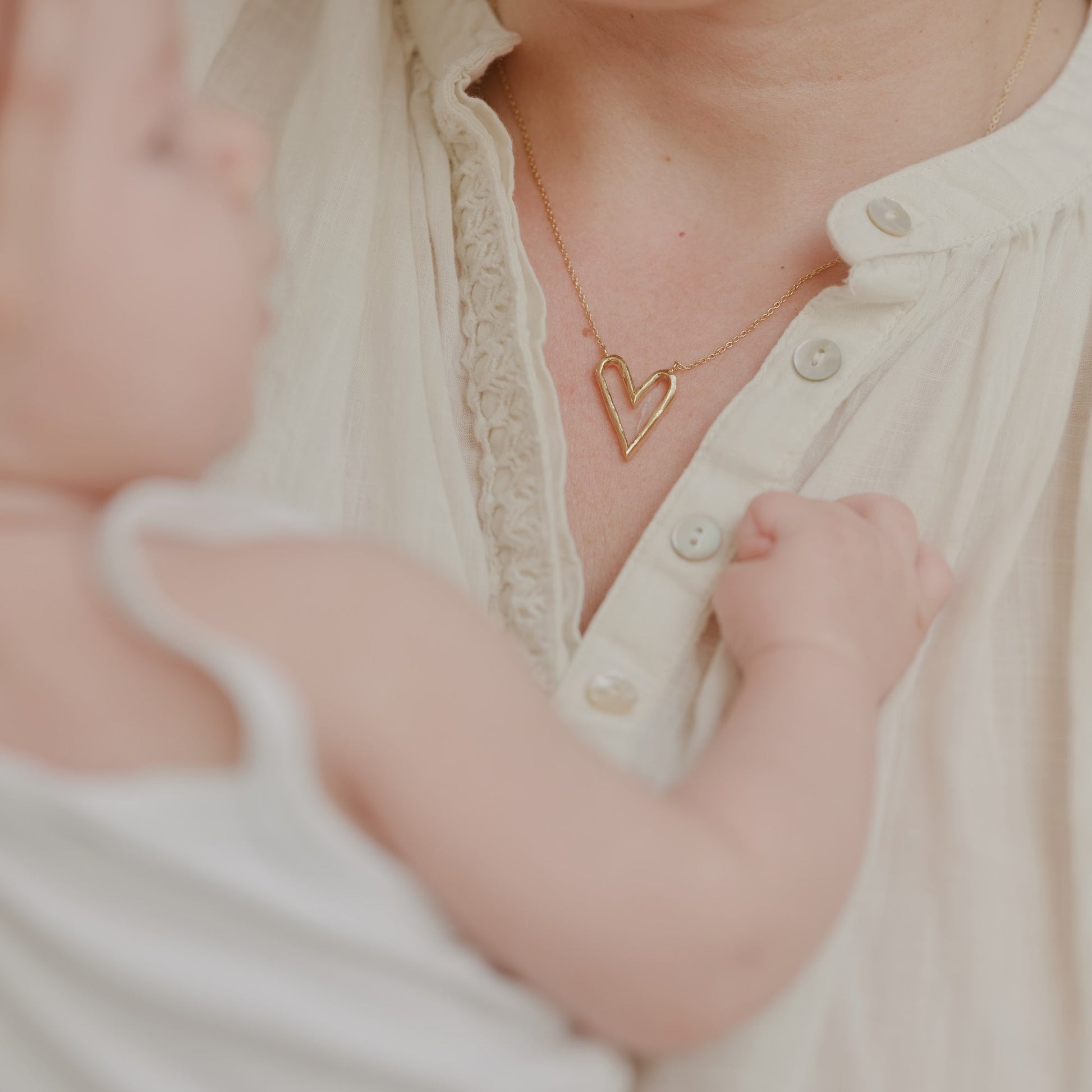 Woman holding wearing a Aurore Havenne gold heart necklace with a blurred background